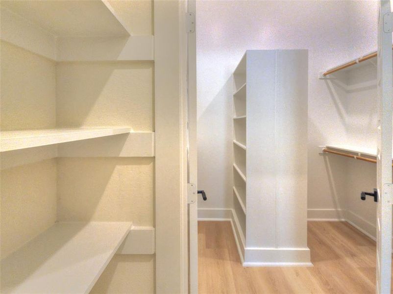 Walk-in closet featuring extensive built-in shelving, wood-finish flooring, and white baseboards
