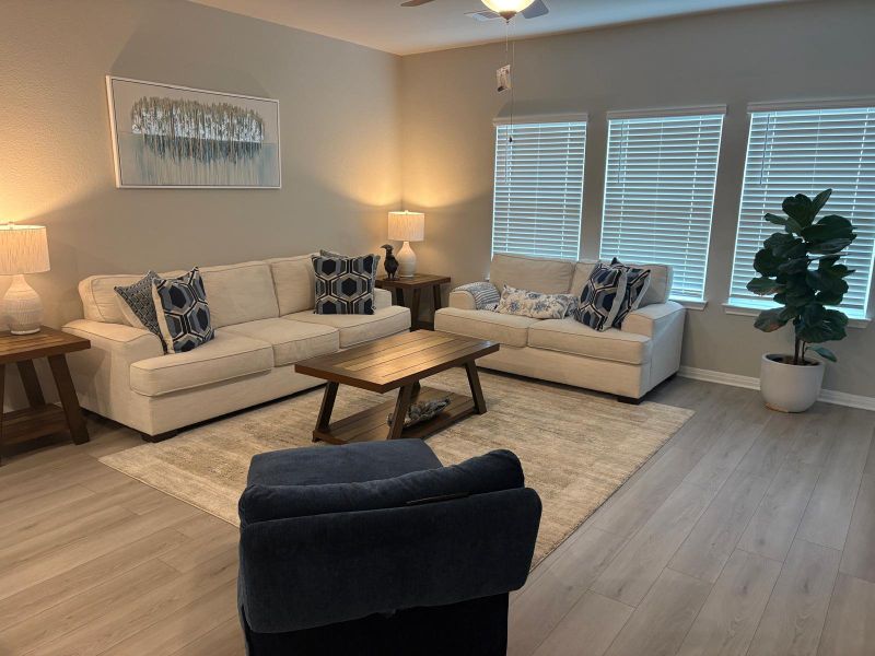 A well-lit living area showcases light-toned flooring and multiple windows, providing a comfortable gathering space.