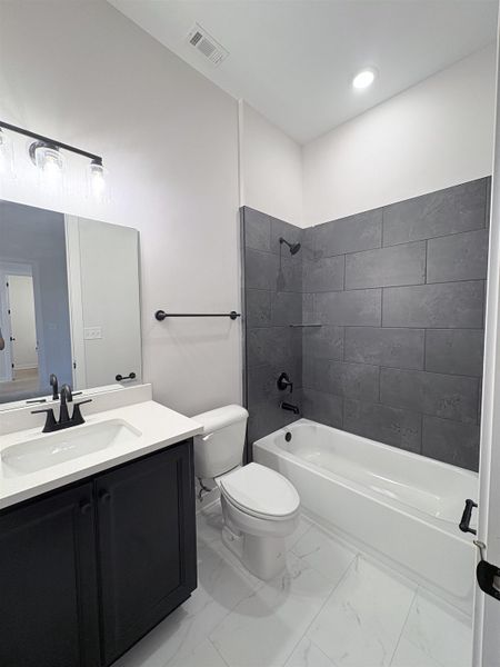 White tile flooring, dark gray subway tile shower surround, single vanity with black cabinetry, white countertop with integrated sink, and matte black hardware White tile flooring, dark gray subway tile shower surround, single vanity with black cabinetry, white countertop with integrated sink, and matte black hardware