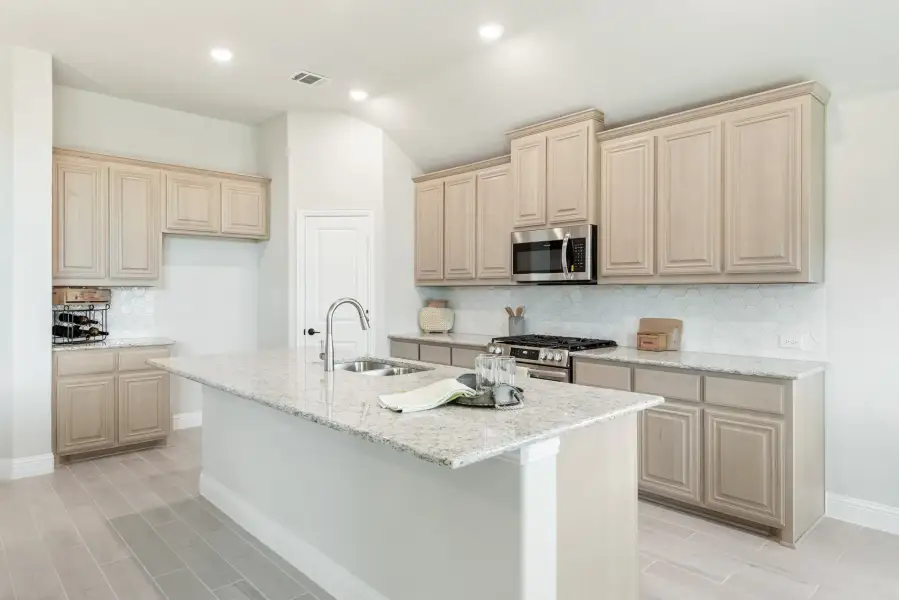 Kitchen with light wood cabinets, granite island with sink, and stainless steel appliances on tile floors