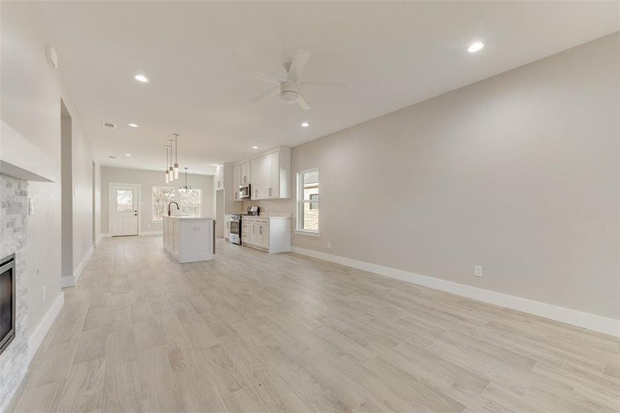 Unfurnished living room with a stone fireplace, plenty of natural light, ceiling fan, and light hardwood / wood-style floors