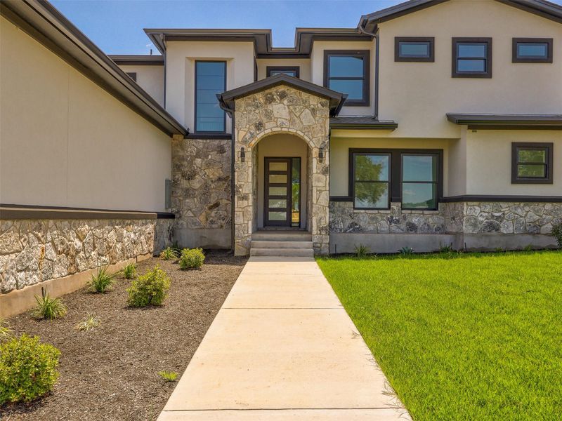 An arched stone entryway highlights the modern stucco exterior of this luxury home.