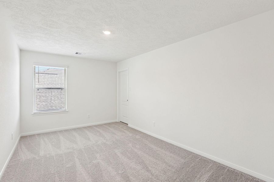 This secondary bedroom offers comfort and style with plush carpeting, neutral paint tones, recessed lighting, a large window with blinds, and a walk-in closet.