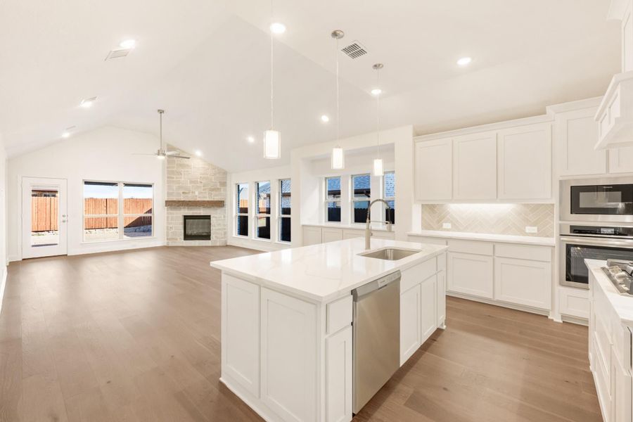 Open kitchen with white cabinets, center island, and hardwood floors, open to living room with stone fireplace Open kitchen with white cabinets, center island, and hardwood floors, open to living room with stone fireplace