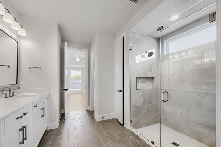 Spacious bathroom featuring a frameless glass shower enclosure with a built-in niche, white vanity with stone-finish countertop and undermount sink, and wood-look tile flooring