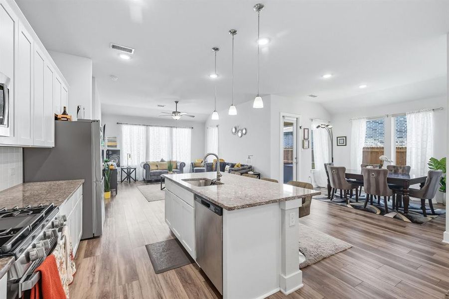 Kitchen featuring open floor plan, white cabinets, light stone counters, pendant lighting, and light wood-style flooring Kitchen featuring open floor plan, white cabinets, light stone counters, pendant lighting, and light wood-style flooring
