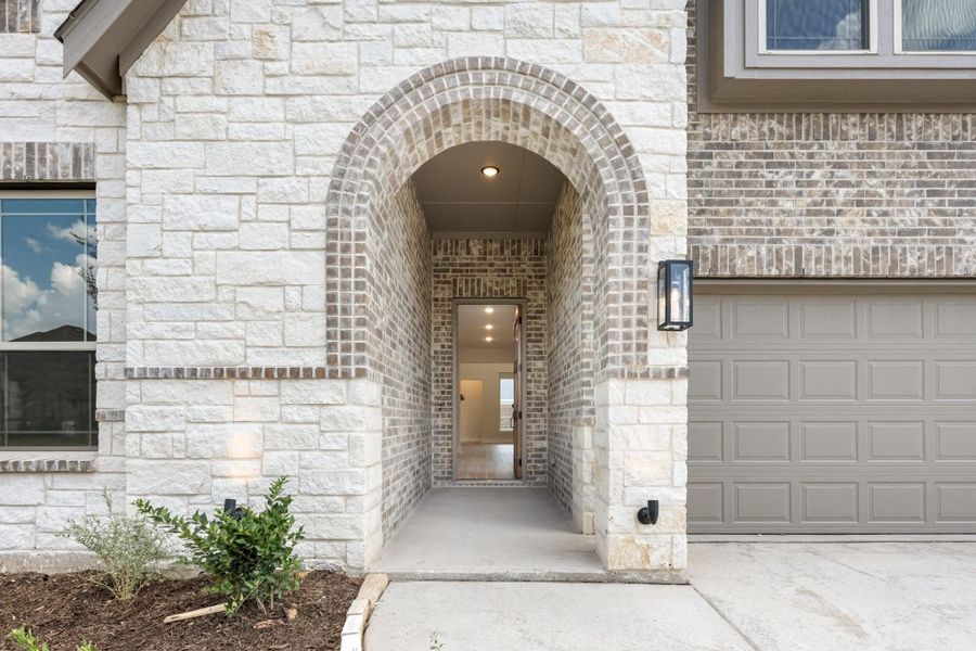 Home entrance with arched brick entryway, stone exterior, and garage door visible to the right