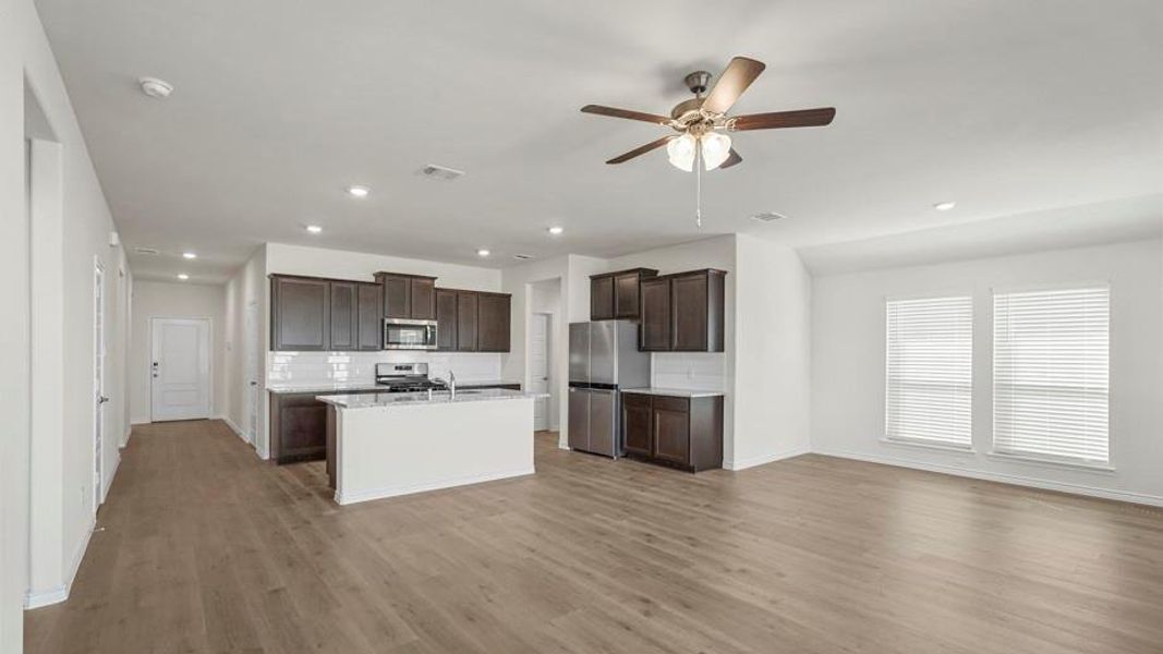 This open-concept living space features light wood-style flooring, a kitchen with dark cabinetry, stainless steel appliances, and a central island