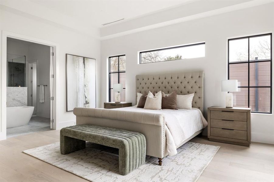 Bedroom featuring light wood finished floors, baseboards, visible vents, and ensuite bathroom