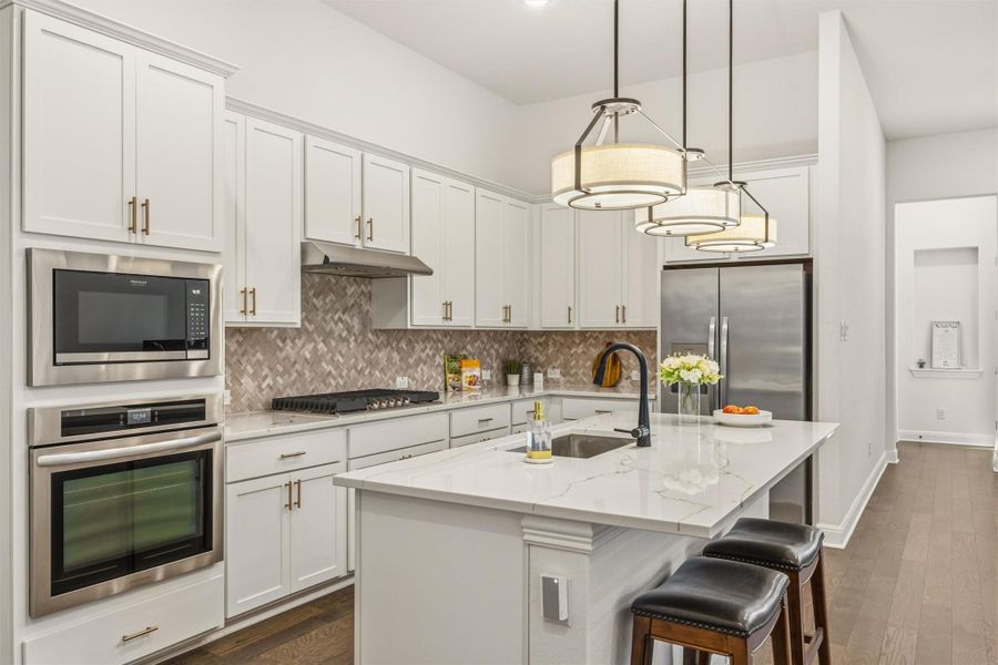 Kitchen featuring appliances with stainless steel finishes, light stone counters, backsplash, and a center island with sink