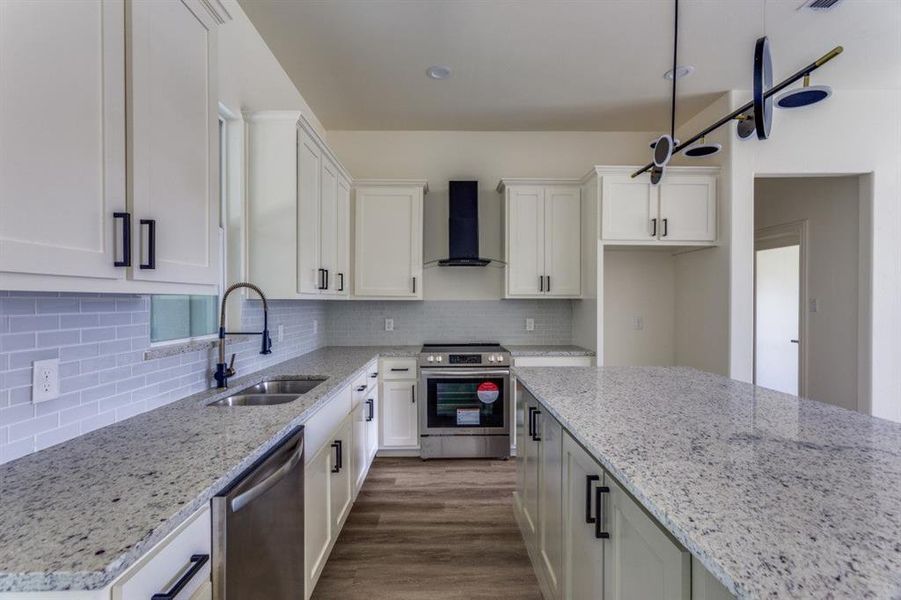 Kitchen featuring stainless steel appliances, wall chimney exhaust hood, a sink, white cabinetry, and light stone counters