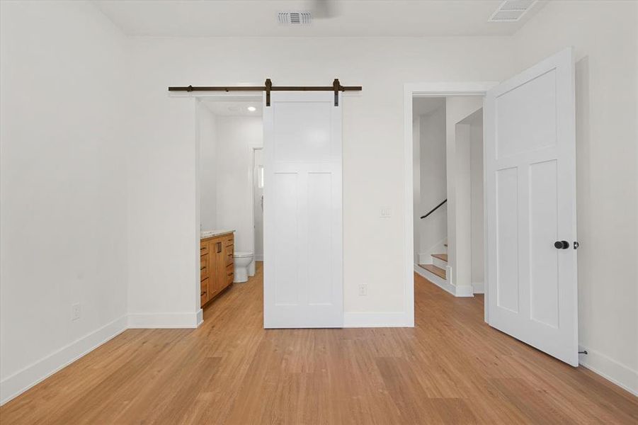 Unfurnished bedroom with a barn door, light wood-type flooring, and ensuite bath