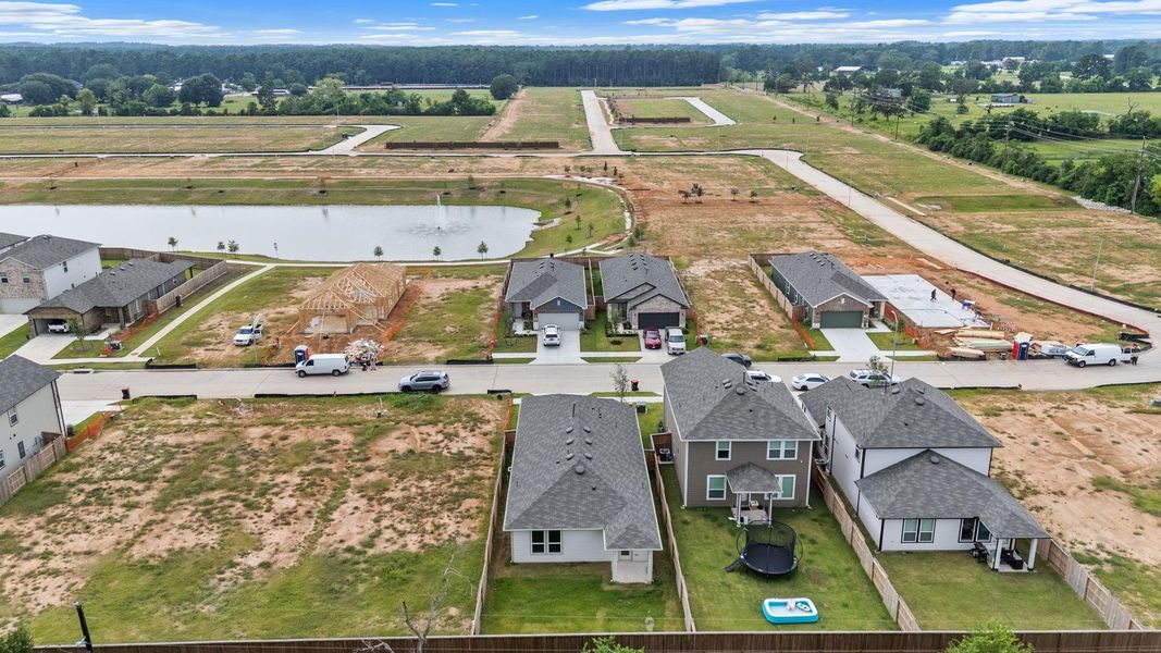 This aerial perspective highlights the prime location of this house, ideally situated just steps from a scenic pond with a fountain. Located in a growing new-construction community, this home offers a tranquil backdrop with no rear neighbors and expansive green space behind.