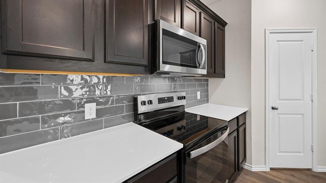 Kitchen featuring dark cabinetry, white countertops, a stainless steel microwave, a stainless steel range, and a gray subway tile backsplash Kitchen featuring dark cabinetry, white countertops, a stainless steel microwave, a stainless steel range, and a gray subway tile backsplash