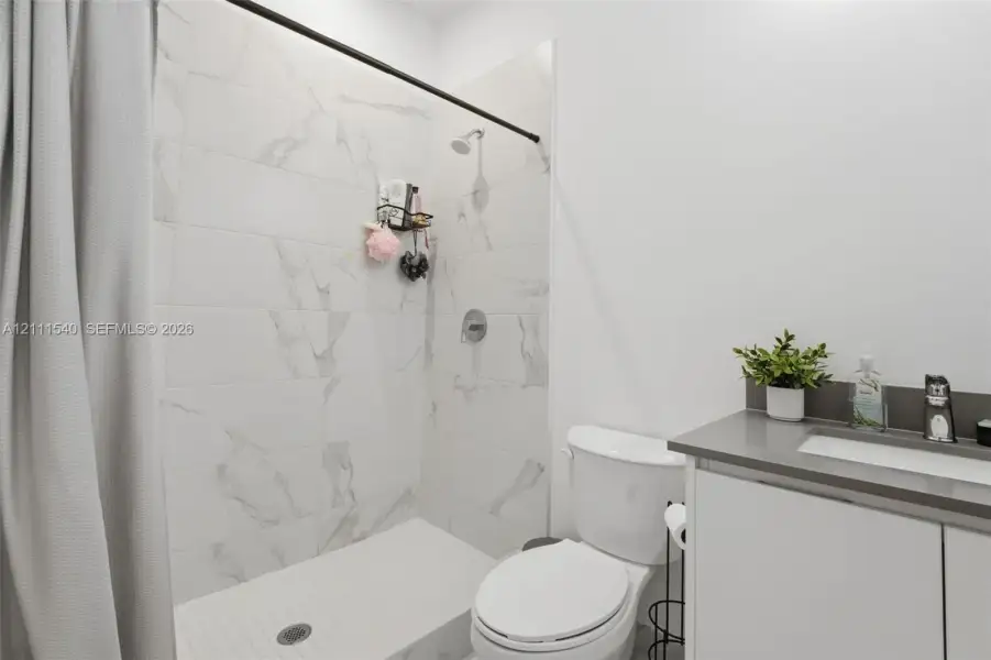 Shower enclosure featuring large-format veined tile surround, matte black shower hardware, and vanity with stone-finish countertop and integrated sink