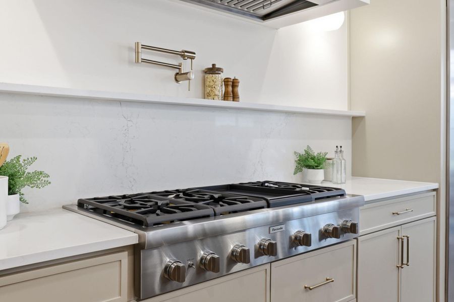 Kitchen with stainless steel gas stovetop, decorative backsplash, and light stone countertops