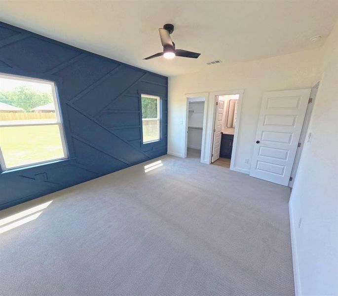 Unfurnished bedroom featuring carpet, a spacious closet, a ceiling fan, a decorative wall, and connected bathroom Unfurnished bedroom featuring carpet, a spacious closet, a ceiling fan, a decorative wall, and connected bathroom