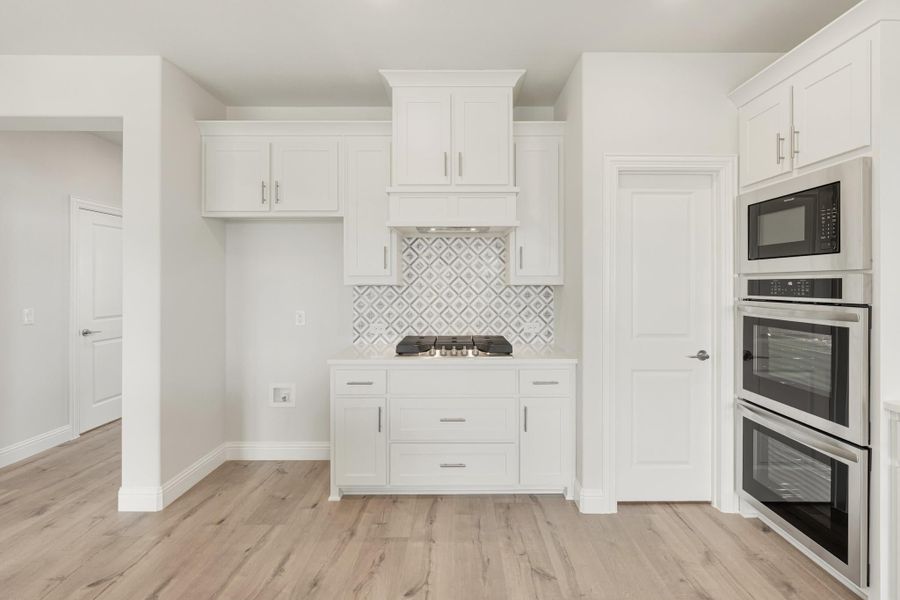 Kitchen with white cabinets, patterned tile backsplash, gas cooktop, and built-in double oven with microwave