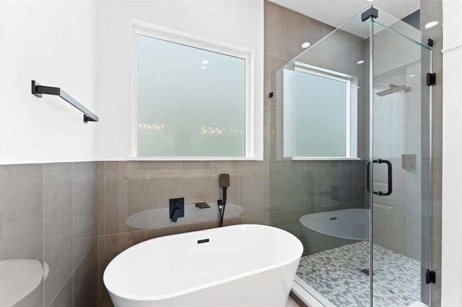 This bathroom features a modern design with a freestanding bathtub and a sleek glass-enclosed shower. It has a neutral color palette with frosted windows for privacy and stylish black fixtures for a contemporary touch.