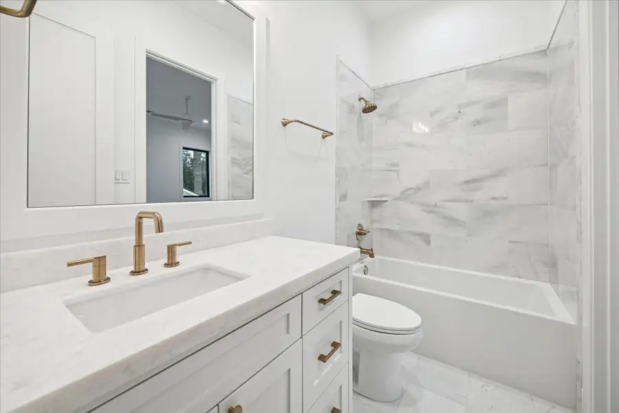 Crisp white finishes, streamlined brass fixtures, and large-format tile give this en-suite bath a bright, contemporary look with clean architectural lines.