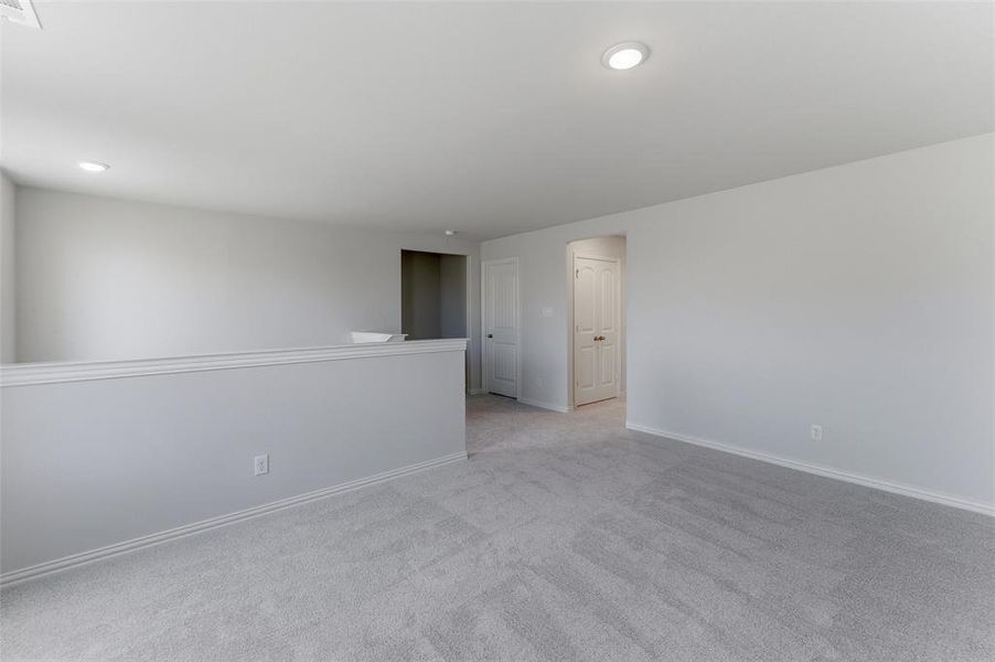 Spacious carpeted loft area with recessed lighting and neutral wall tones
