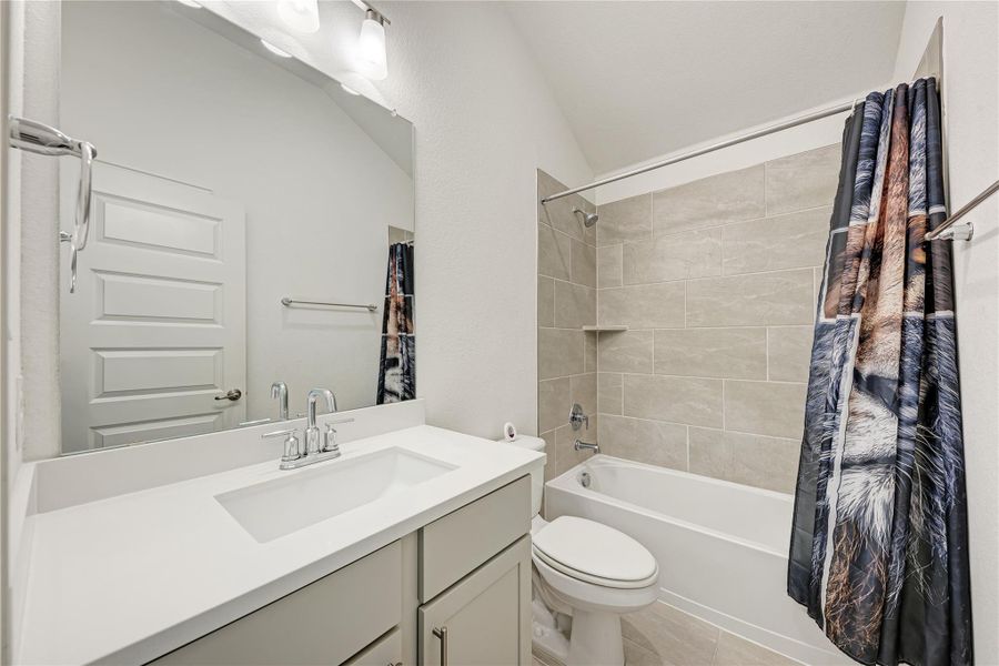 A pristine bathroom features a modern vanity with a wide sink and an immaculate tiled shower-tub combination.
