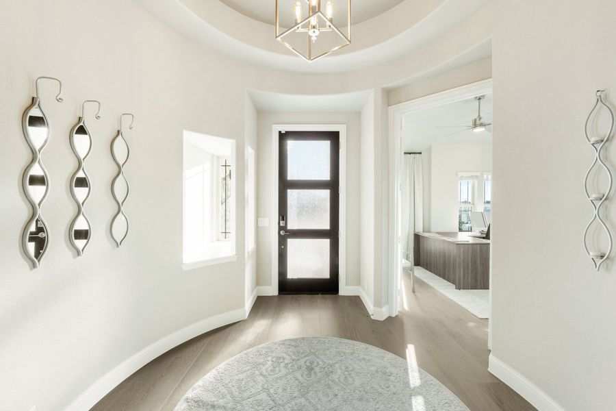 Rounded foyer with tray ceiling, geometric chandelier, dark glass front door, and hardwood floors Rounded foyer with tray ceiling, geometric chandelier, dark glass front door, and hardwood floors