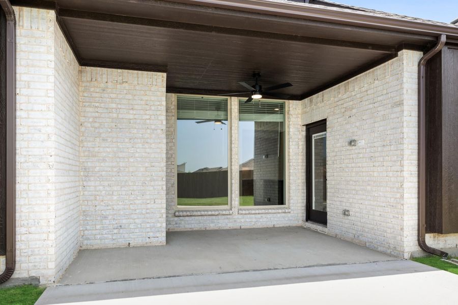 Covered back patio with ceiling fan, white brick walls, and concrete floor Covered back patio with ceiling fan, white brick walls, and concrete floor