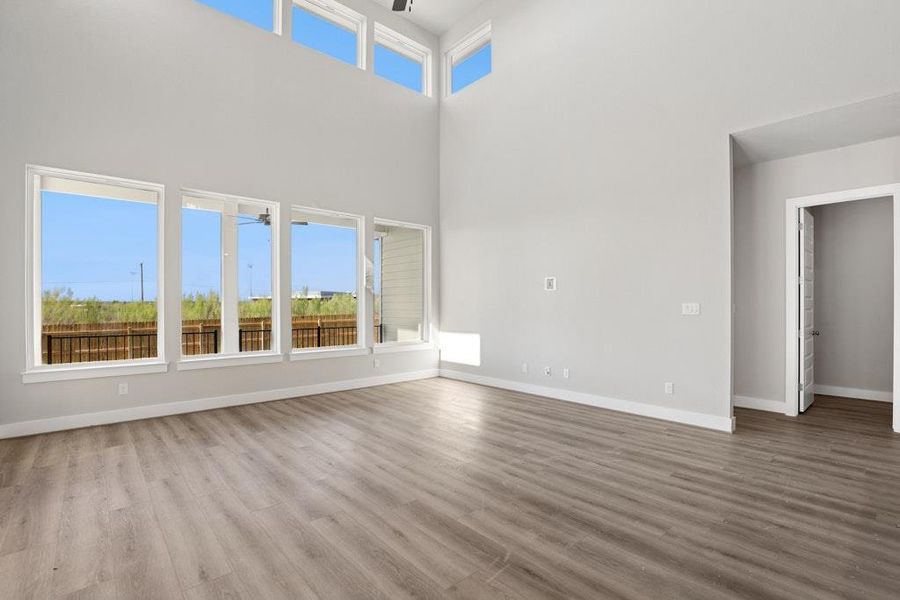Unfurnished room with plenty of natural light, ceiling fan, light wood-style flooring, and a high ceiling Unfurnished room with plenty of natural light, ceiling fan, light wood-style flooring, and a high ceiling