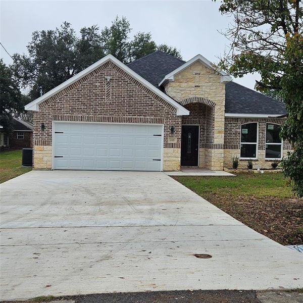 View of front of property with stone siding, a shingled roof, concrete driveway, and an attached garage