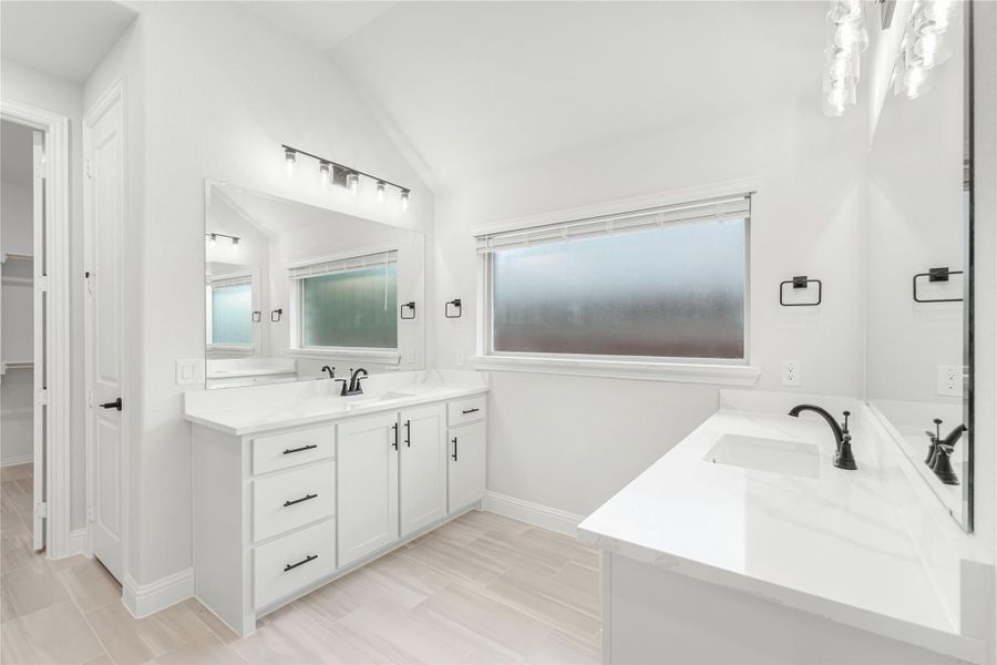 Master bathroom with white double vanity, soaking tub, and vaulted ceiling with black hardware accents Master bathroom with white double vanity, soaking tub, and vaulted ceiling with black hardware accents