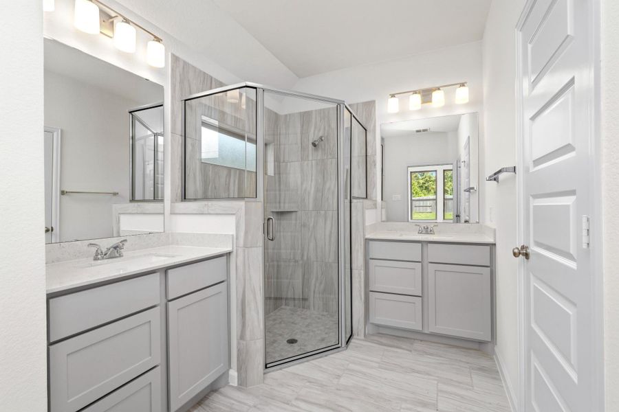 Primary bathroom with dual vanities and oversized glass-enclosed tiled shower.