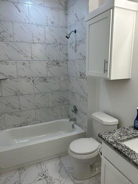 Full bathroom featuring vanity, tiled shower/bath combo, and toilet