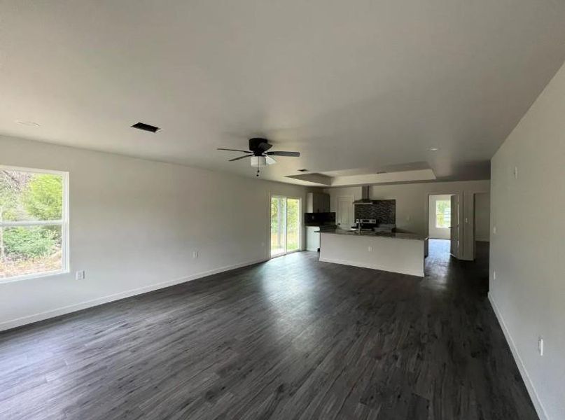 Unfurnished living room featuring dark wood finished floors, a wood stove, ceiling fan, and a raised ceiling