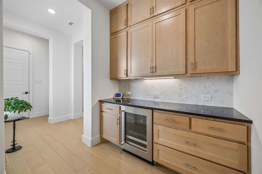 Bar featuring beverage cooler, light wood-style floors, light wood finish cabinets, recessed lighting, and tasteful backsplash
