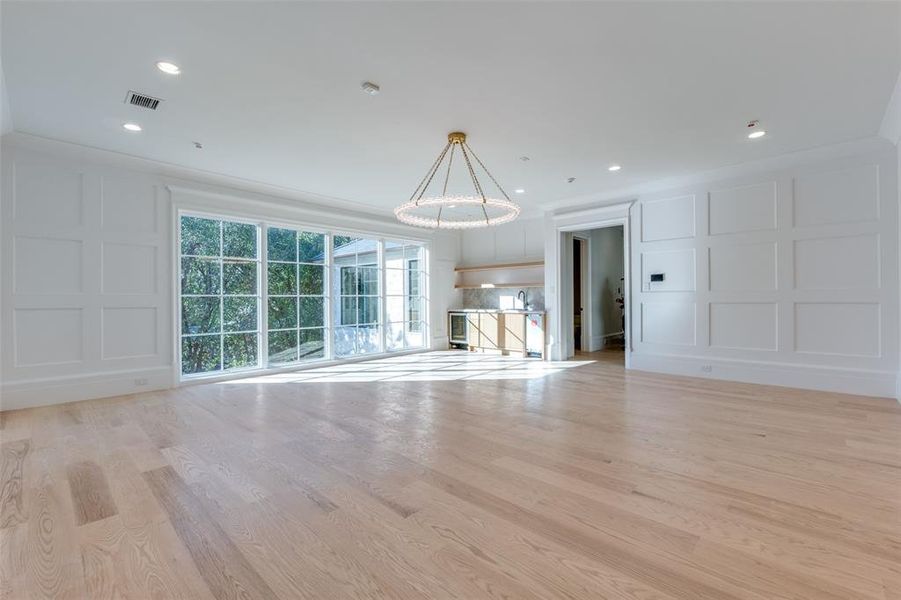 Unfurnished living room with light wood-type flooring, an inviting chandelier, and ornamental molding