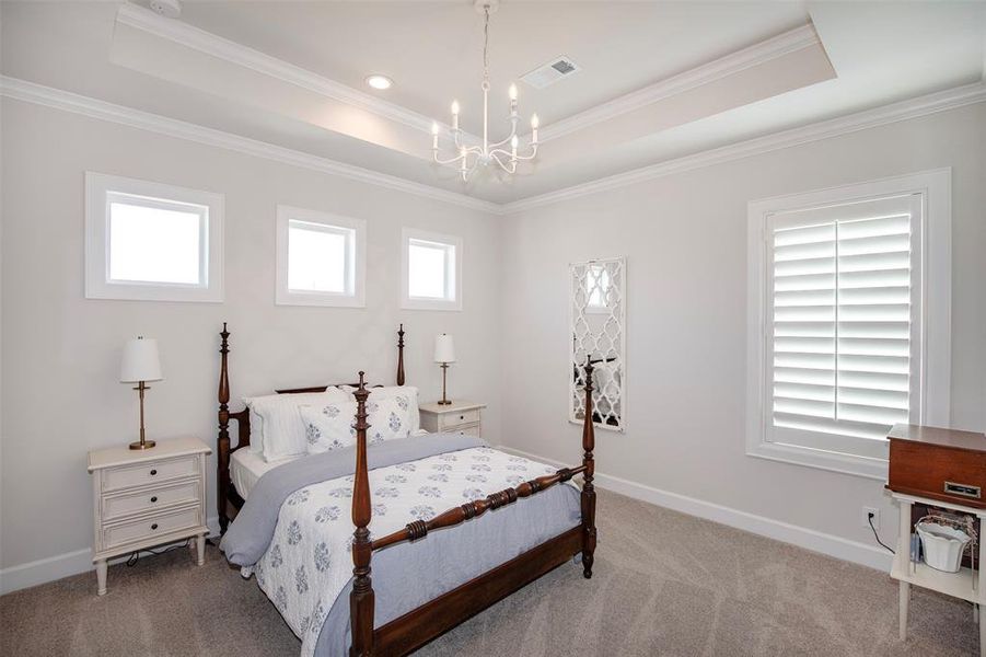 This bedroom features a cozy four-poster bed with elegant bedding, flanked by two bedside tables with lamps. It has a bright, airy feel with three small windows and a larger window with shutters. The room is accented by a decorative mirror and a modern chandelier, creating a serene and stylish atmosphere.