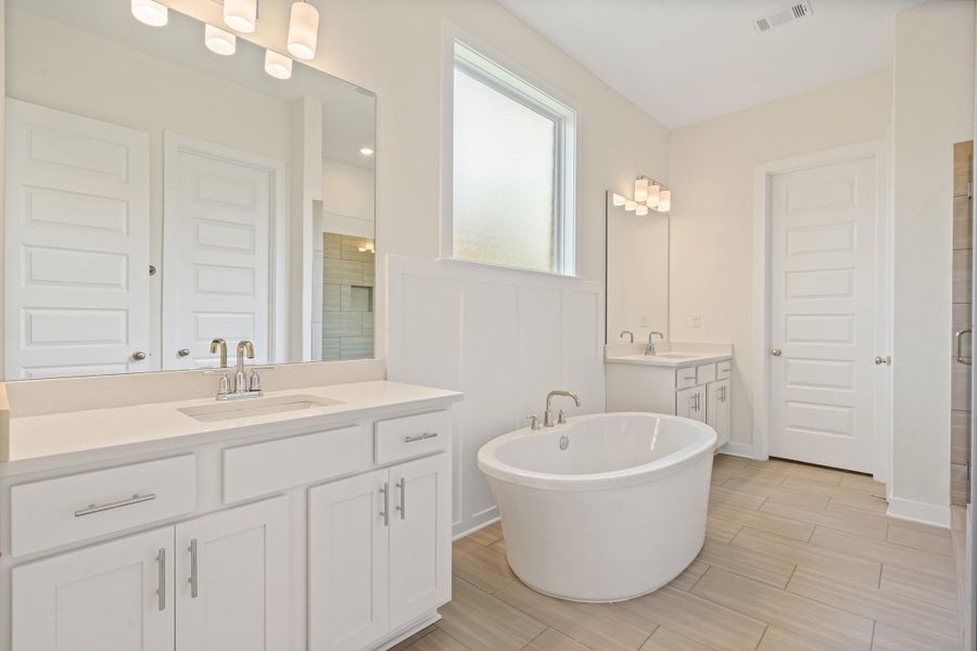 Spacious bathroom featuring a freestanding oval tub, dual vanities with white cabinetry and light-toned countertops, and wood-finish flooring Spacious bathroom featuring a freestanding oval tub, dual vanities with white cabinetry and light-toned countertops, and wood-finish flooring