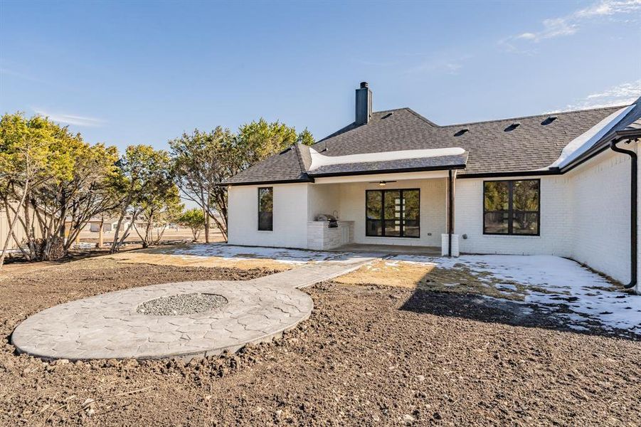Rear view of property featuring a patio area, roof with shingles, a chimney, brick siding, and a ceiling fan