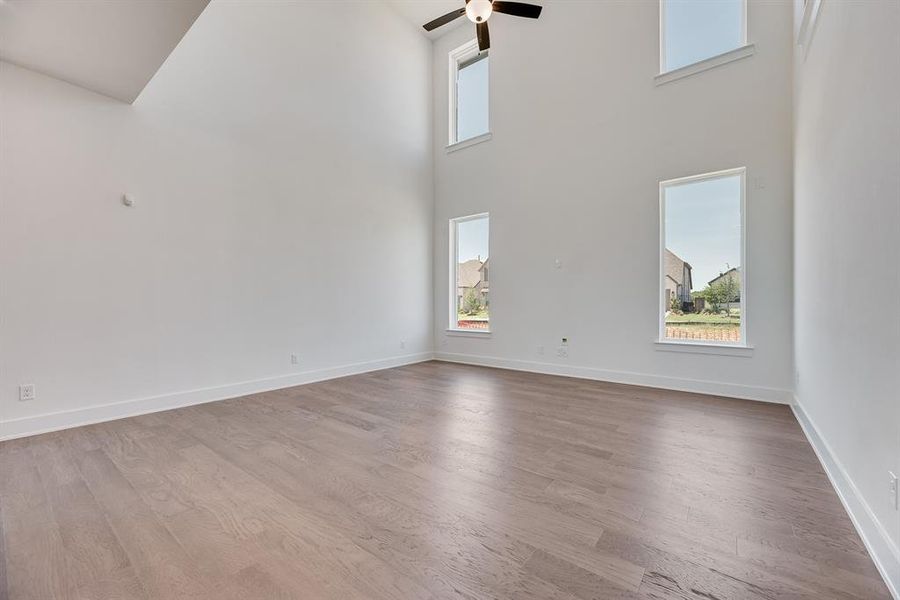 Unfurnished living room with wood finished floors, a high ceiling, and a ceiling fan Unfurnished living room with wood finished floors, a high ceiling, and a ceiling fan