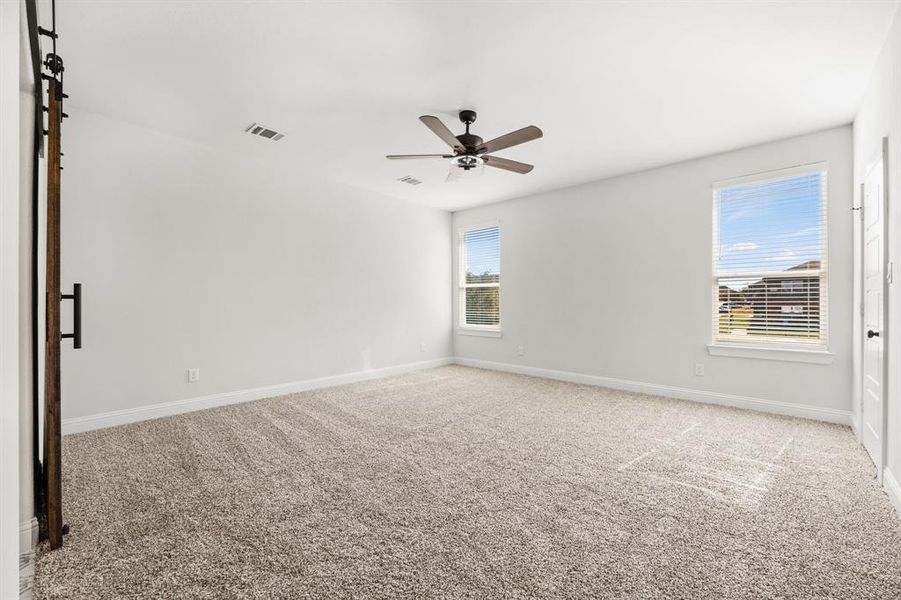 Empty room with light carpet, a barn door, and ceiling fan