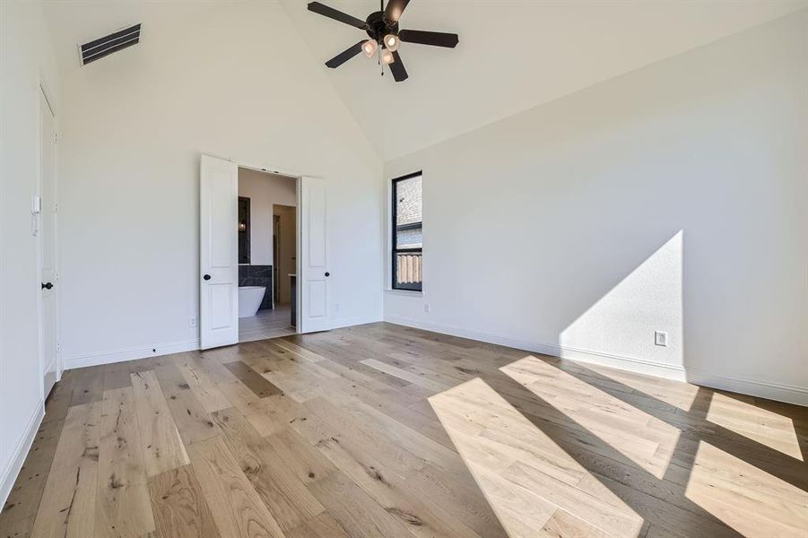 Empty room featuring high vaulted ceiling, ceiling fan, and light hardwood / wood-style floors