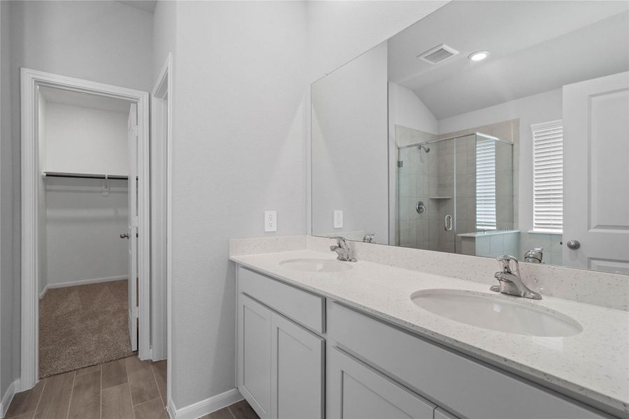 A bright and functional primary bath offering dual sinks for busy mornings, a large mirror, soaking tub, and a modern glass-enclosed shower, creating a serene and efficient space.
