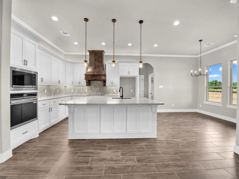 Kitchen featuring white cabinetry, crown molding, stainless steel oven, light stone countertops, and wood tiled floors Kitchen featuring white cabinetry, crown molding, stainless steel oven, light stone countertops, and wood tiled floors