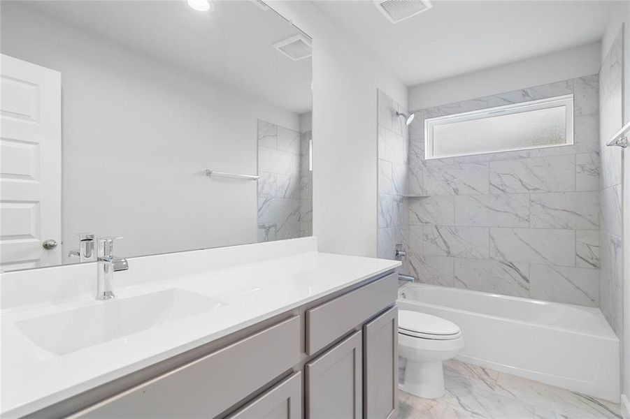 Secondary bath features tile flooring, bath/shower combo with tile surround, stained wood cabinets, beautiful light countertops, mirror, sleek fixtures and modern finishes.