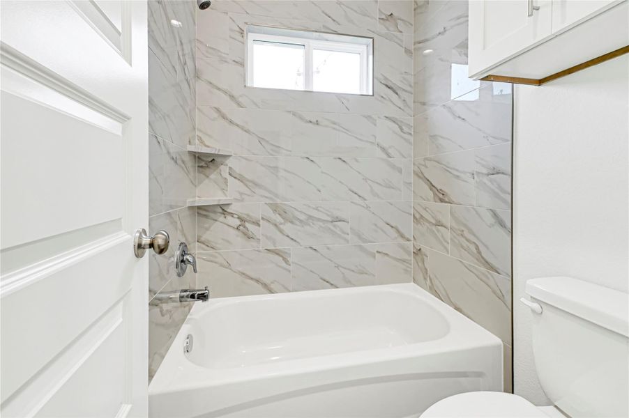 Bright and modern bathroom featuring a sleek bathtub with marble-style tile walls, a small window for natural light, and a convenient built-in shelf. Bright and modern bathroom featuring a sleek bathtub with marble-style tile walls, a small window for natural light, and a convenient built-in shelf.