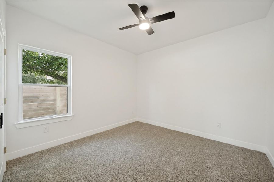 Comfortable carpeted bedroom features a window overlooking lush greenery and a modern ceiling fan. Comfortable carpeted bedroom features a window overlooking lush greenery and a modern ceiling fan.