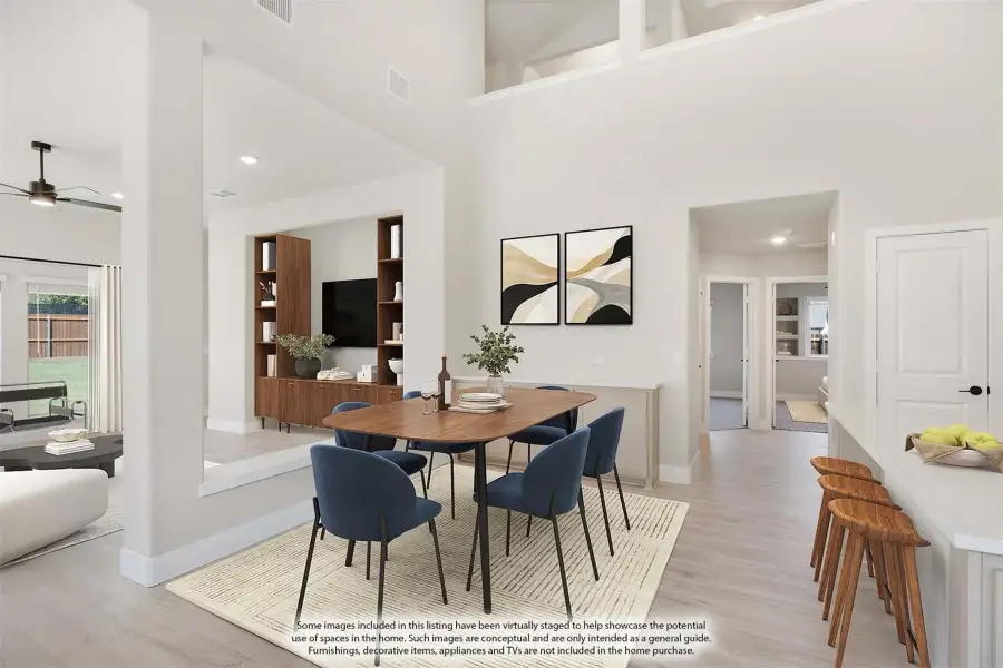 Open-concept dining area with high ceilings, wood table, blue chairs, and view into living room and kitchen