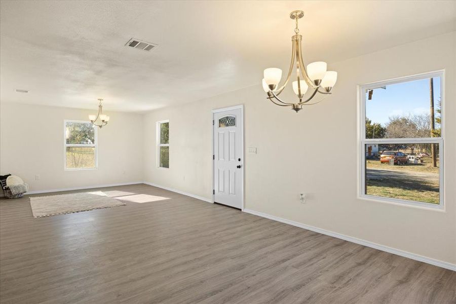 Spare room featuring wood-type flooring, a wealth of natural light, and an inviting chandelier