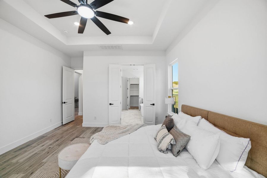 Bedroom featuring a raised ceiling, wood finished floors, ceiling fan, recessed lighting, and a walk in closet Bedroom featuring a raised ceiling, wood finished floors, ceiling fan, recessed lighting, and a walk in closet
